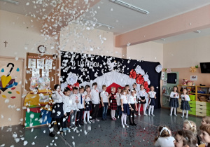 Dzieci na tle dekorcji recytują wiersz,podczas którego wystrzelono biało- czerwone konfetti