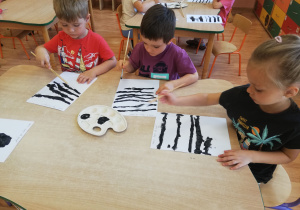 Dzieci malują poprzeczne pasy czarną farbą, tworząc przejście dla pieszych
