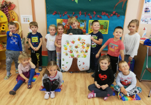 Dzieci pozują do zdjęcia z wykonaną pracą plastyczną, przedstawiającą drzewo