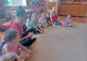Dzieci siedzą na dywanie z instruktorem tańca