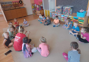 Dzieci siedzą w kole na dywanie z instruktorem tańca