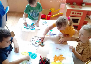 Dzieci przy stoliku stemplują pracę farbą