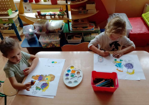 Dzieci kolorują kredkami i malują farbami przy stoliku