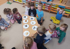 Dzieci siedzą wokół stołu na którym rozłożone są talerzyki z suszonymi owocami