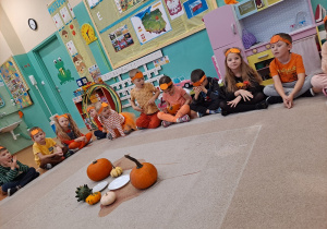 Dzieci siedzą na dywanie podczas omawiania wyglądu dyni