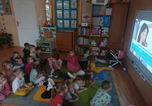 Dzieci siedzą na dywanie i dopowiadają na pytania quizowe