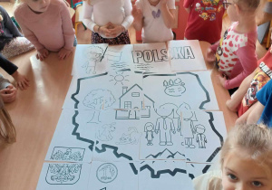 Dzieci stoją wokół stołu na którym ułożyły kolorowankę dotycząca Polski