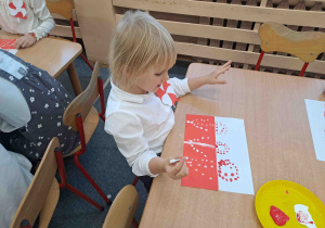 Dzieci wykonują pracę plastyczną, malują patyczkami kosmetycznymi na biało - czerwonych kartkach "Kwiaty dla Niepodległej"