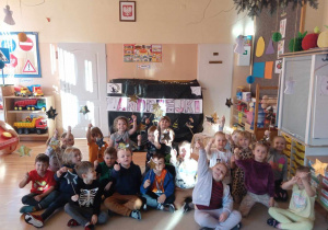 Dzieci siedzą na tle dekoracji andrzejkowych i pokazują wykonane przez siebie magiczne różdżki.