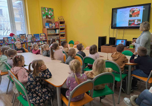 Dzieci w bibliotece słuchają opowieści pani i oglądają prezentację multimedialną dotyczącą Świętego Mikołaja