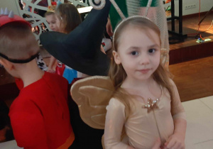Dziewczynka przebrana za motylka na balu karnawałowym. w tle widać dzieci siedzące.