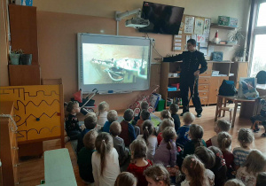 Dzieci siedzą na dywanie i oglądają film na tablicy multimedialnej na temat pracy w kopalni.