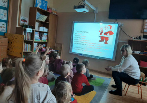 Dzieci oglądają film edukacyjny na tablicy multimedialnej nt Świętego Mikołaja. Pani opowiada dzieciom jak w innym państwie spędzane są Święta Bożego Narodzenia.