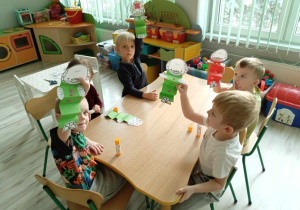 Chłopcy przy stole prezentują samodzielnie wykonaną pracę z papieru.