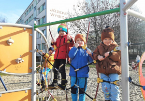 Trzech chłopców wspina się po ściance sznurkowej na placu zabaw.