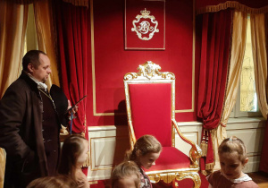 Pan przewodnik pokazuje dzieciom tron Króla Augusta.