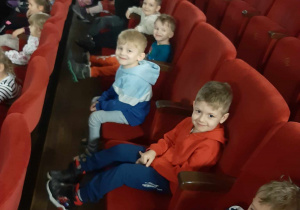 Dzieci siedzą w fotelach w sali kinowej.