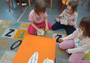 Dzieci przyklejają swoje garnuszki tworząc wspólny plakat ilustrujący przysłowie "W marcu jak w garncu"