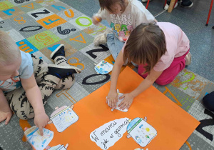 Dzieci przyklejają swoje garnuszki tworząc wspólny plakat ilustrujący przysłowie "W marcu jak w garncu"