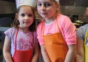 Dziewczynki pozują do zdjęcia w czapkach kucharskich i fartuszkach.