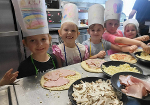 Dziewczynki w czapkach kucharskich przy pizzy.