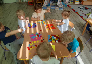 Dzieci układają płaskie figury geometryczne tworząc niepowtarzalne kolorowanki.