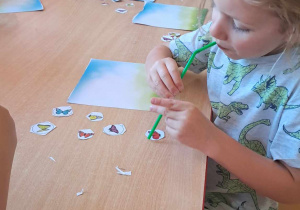 Dzieci przy pomocy słomki umieszczają motyle na łące