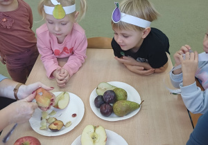 Dzieci obserwują jak nauczyciel obiera gruszkę ze skórki