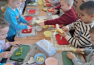 Dzieci przy stoliczkach kroją owoce i warzywa do koktajlu