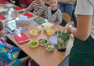 Dzieci przy stoliczkach kroją owoce i warzywa do koktajlu