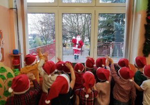 Dzieci stoją przed oknem i obserwują Mikołaja, który chodzi po przedszkolnym tarasie