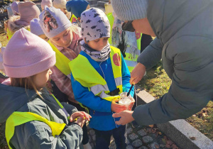 Dzieci zapalają znicze z pomocą nauczycielki