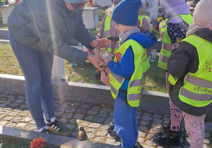 Dzieci zapalają znicze z pomocą nauczycielki