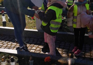 Dzieci zapalają znicze z pomocą nauczycielki