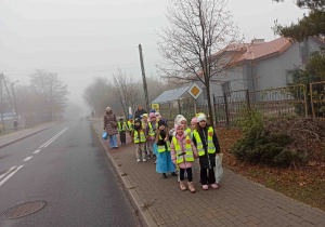 Dzieci ubrane w kamizelki odblaskowe idą ulicą.