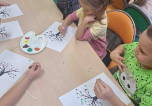 Dzieci malują kolorowe liście używając patyczków higienicznego.