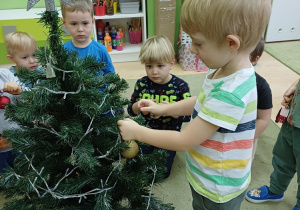 Dzieci ubierają choinkę w sali przedszkolnej