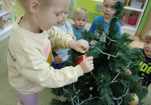 Dzieci ubierają choinkę w sali przedszkolnej