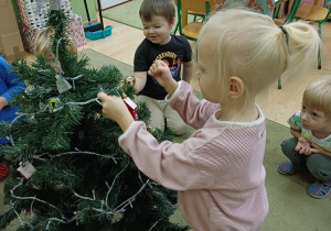 Dzieci ubierają choinkę w sali przedszkolnej