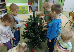 Dzieci ubierają choinkę w sali przedszkolnej