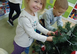 Dzieci ubierają choinkę w sali przedszkolnej