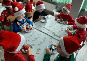 Dzieci siedzą przy stoliku i zajadają babeczki