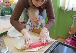 Chłopiec z pomocą nauczyciela wałkuje ciasto na pizzę