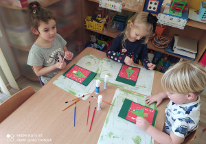 Dzieci dekorują białą farbą karty świąteczne przy drugim stoliku