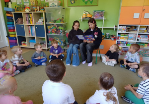 Dzieci z grupy Poziomki siedzą na dywanie i słuchają bajki czytanej przez dwie starsze koleżanki