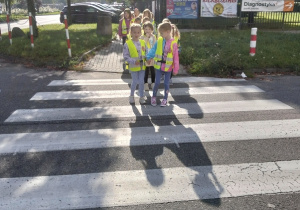 Dzieci przechodzą przez pasy pod czujnym okiem nauczyciela