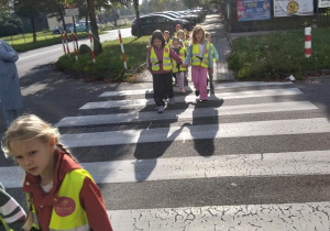 Dzieci przechodzą przez pasy pod czujnym okiem nauczyciela