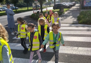 Dzieci przechodzą przez pasy pod czujnym okiem nauczyciela