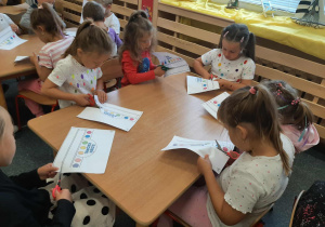 Dzieci siedzą przy stoliku i wycinaja opaski nożyczkami.