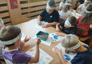 Dzieci siedzą przy stoliku i rysują kropki na kartce.
